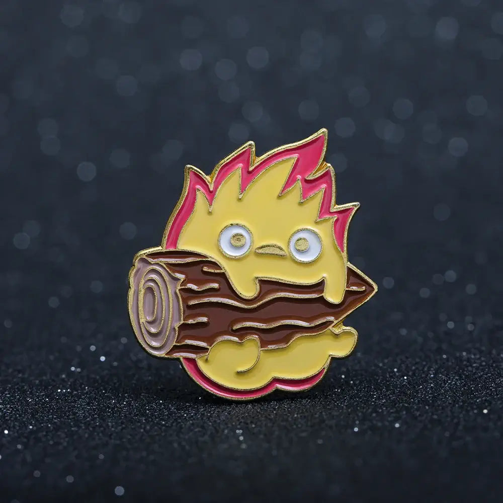 Howls moving castle calcifer enamel pin with yellow and pink flame design and cartoon character behind brown log