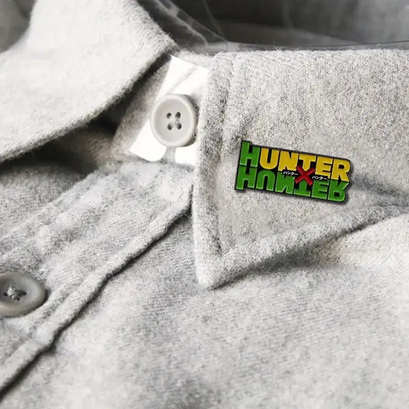 A vibrant green and yellow hunter x hunter logo brooch enamel pin with japanese text on a gray fabric collar fantasy adventure badge