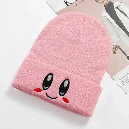 Pink knit kirby plush hat featuring embroidered kawaii eyes and rosy cheeks in soft plush material