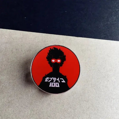 Red and black circular metal brooch featuring kageyama shigeo enamel pin with spiky hair silhouette and glowing red eyes