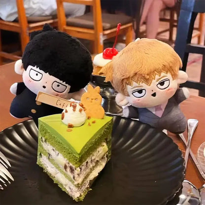 Green layered matcha cake slice topped with white cream chocolate crumbles bunny cookie and cherry beside kageyama shigeo plush keychain bag pendant
