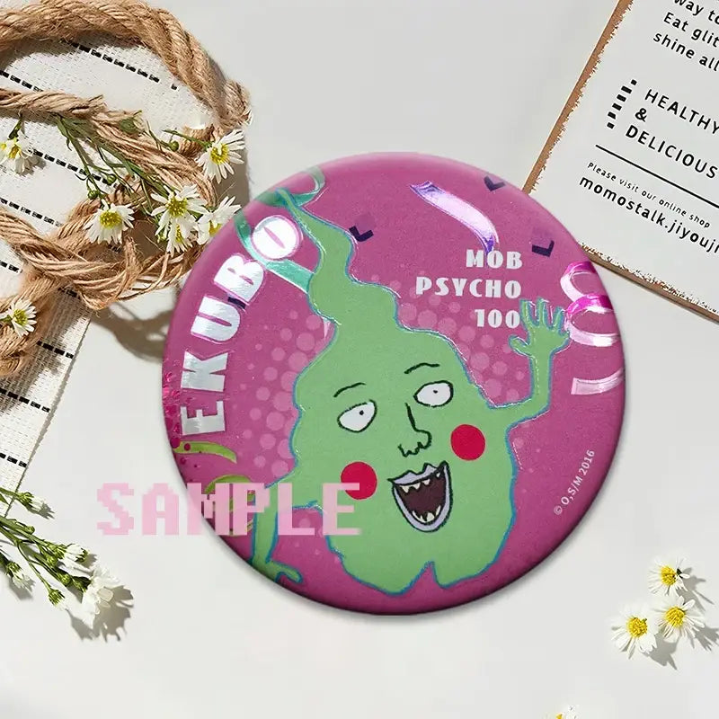 A vibrant pink round kageyama button pin featuring a green cartoon character from mob psycho 100 on a glossy surface