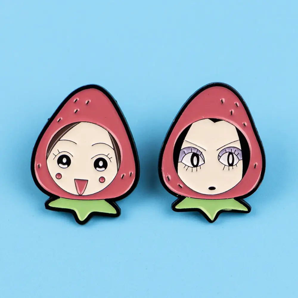 Two strawberry-shaped nana oosaki enamel lapel pins with cartoon faces and pink cheeks on a light blue background