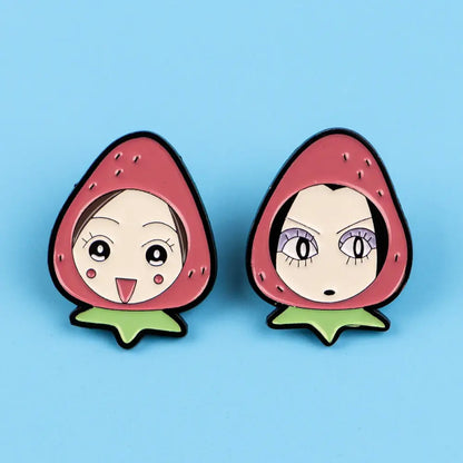 Two strawberry-shaped nana oosaki enamel lapel pins with cartoon faces and pink cheeks on a light blue background