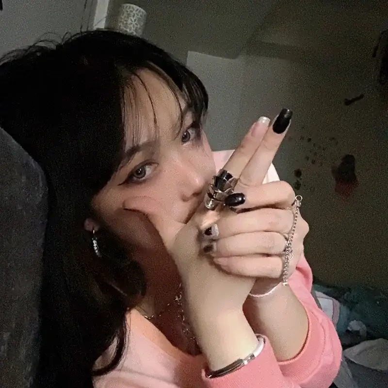 A person wearing a pink top showcases nana oosaki metal armor knuckle rings with black gemstones in a bold style