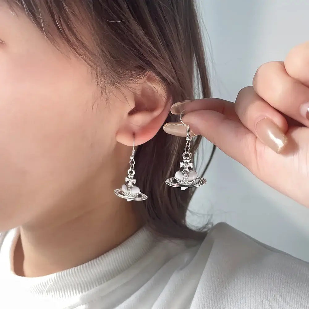 Silver plated saturn planet earrings with white cz heart and bow detail featuring vivienne westwood design