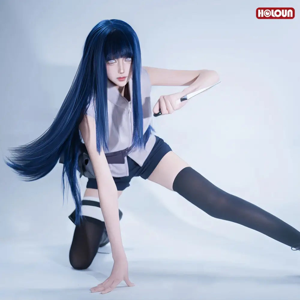 A cosplayer wearing a detailed blue hyuga hinata cosplay wig with a gray blouse, black shorts, and holding a prop knife