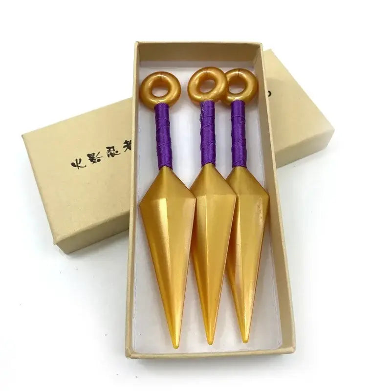 Three golden kunai model knives with purple handles and gold rings in a beige box made of durable pvc
