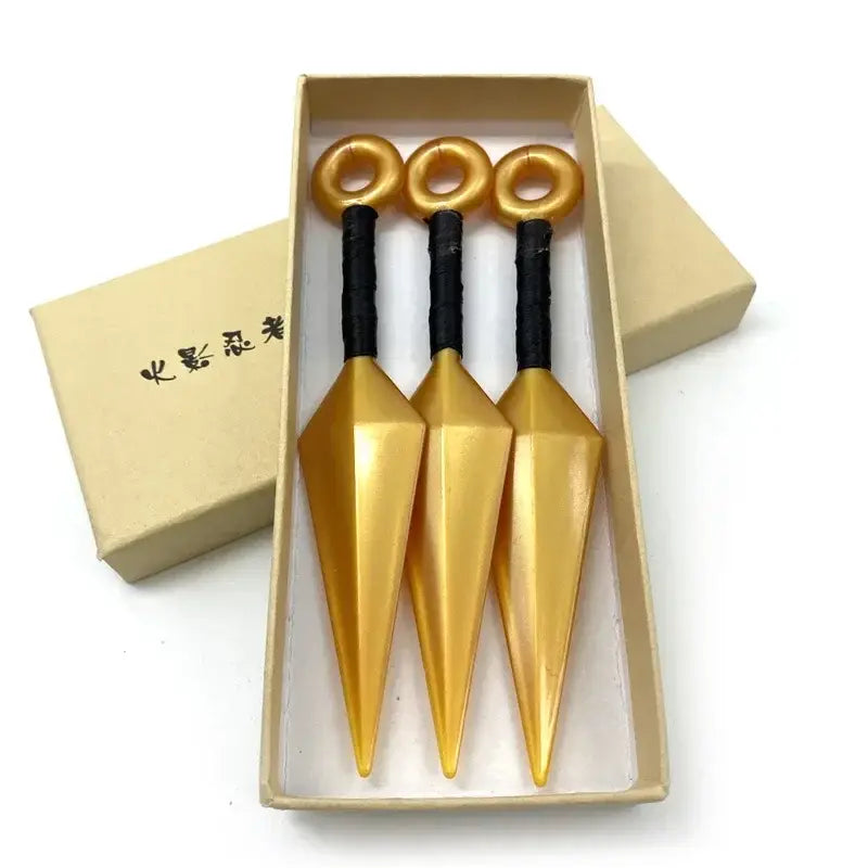 Three golden kunai model knives with black handles made of durable pvc arranged in a beige gift box