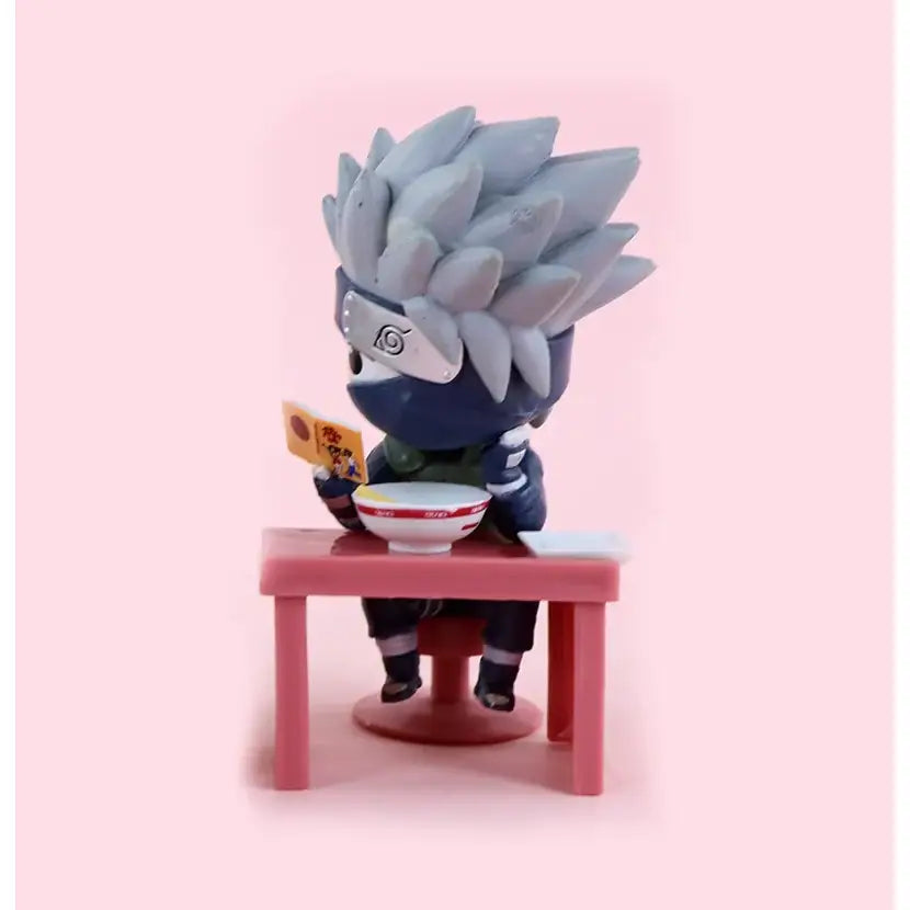 Gray spiky-haired naruto figurine in blue ninja outfit with white headband seated at pink table holding bowl and packet from naruto sasuke blind box figure set