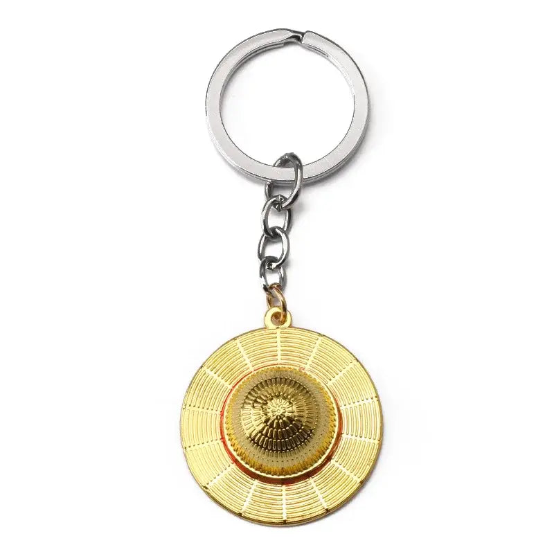 Gold-colored metal luffy hat keychain featuring a detailed circular pendant with concentric ridged patterns and crown design