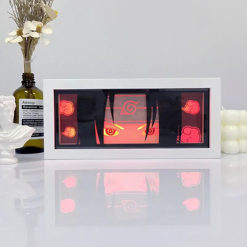 White-framed illuminated naruto uchiha portrait with glowing red eyes and cloud motifs in a shadow box light