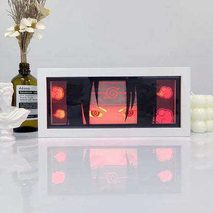 White-framed illuminated naruto uchiha portrait with glowing red eyes and cloud motifs in a shadow box light