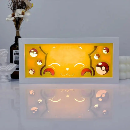 White-framed illuminated pikachu shadow box light with glowing yellow backlight and red poké ball cutout design