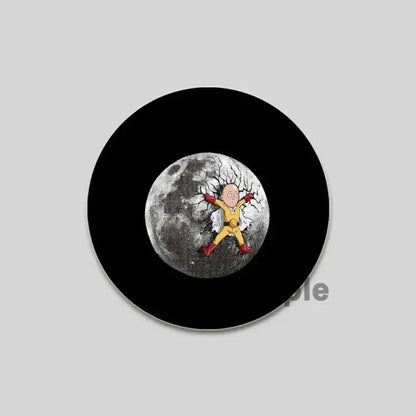 Black circular one punch man saitama brooch pin featuring saitama in yellow suit standing on cracked moon design