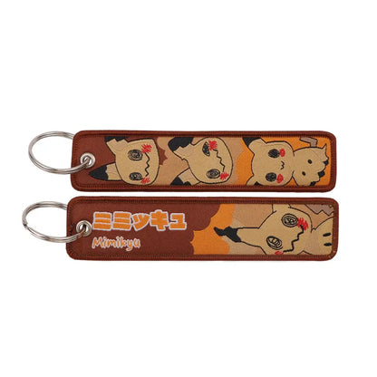 Brown embroidered pokémon mimikyu keychain featuring orange and beige camouflage patterns for jet tag accessory