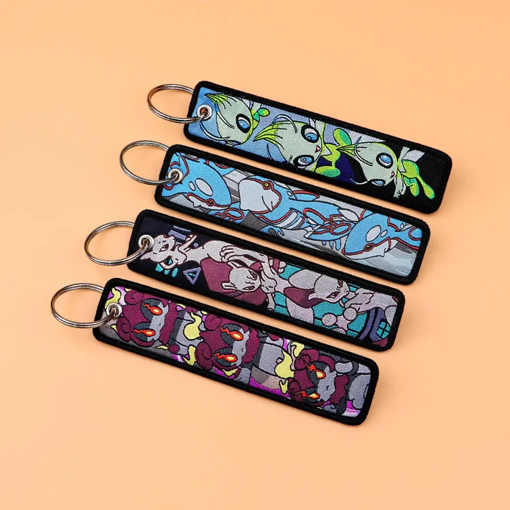 Four rectangular black fabric pokemon pikachu embroidered keychains with colorful cartoon designs and metal rings