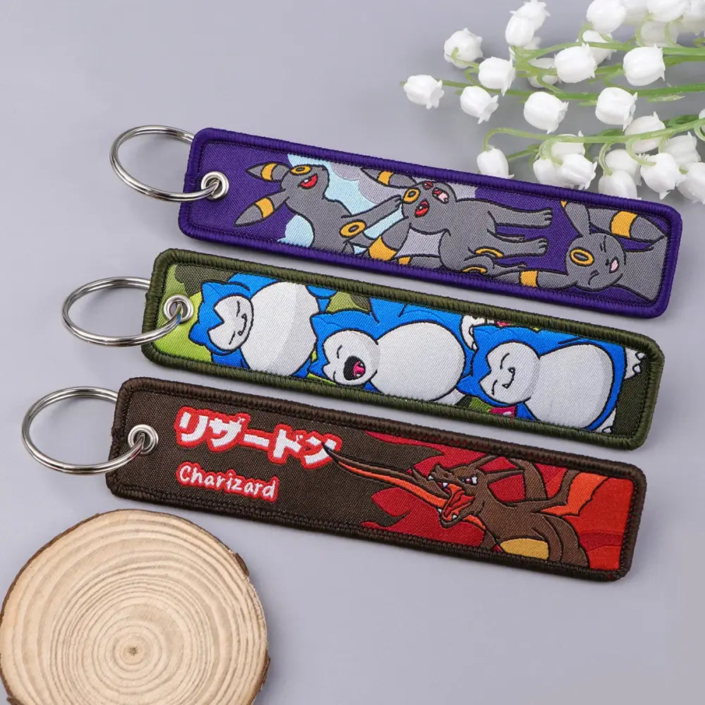 Three colorful embroidered pokémon keychains featuring eevee snorlax and charizard on fabric patches for accessories
