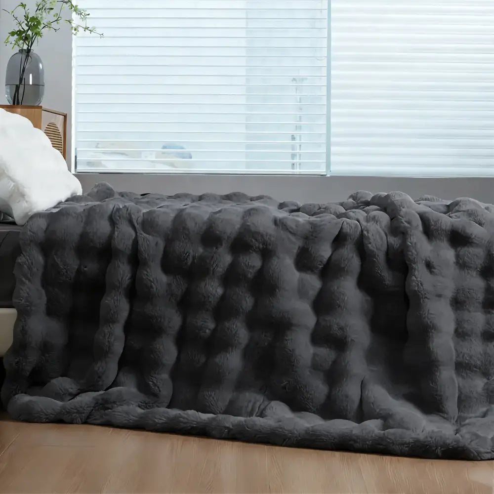 A plush dark gray faux fur rabbit blanket with a cozy thick textured bubble knit pattern for warmth and comfort