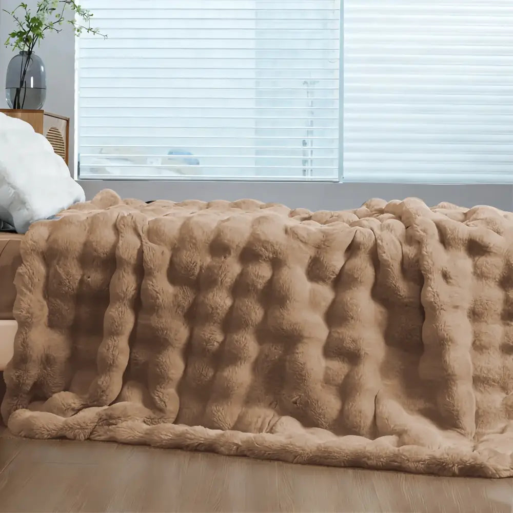 A plush tan-colored faux rabbit fur throw blanket with a soft cozy textured bumpy surface for warmth
