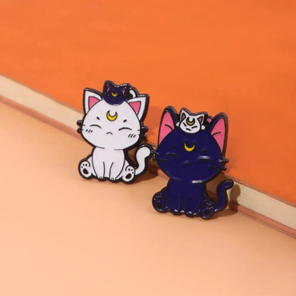 Two enamel keychain brooch pins featuring cartoon cats from sailor moon with white and dark blue colors