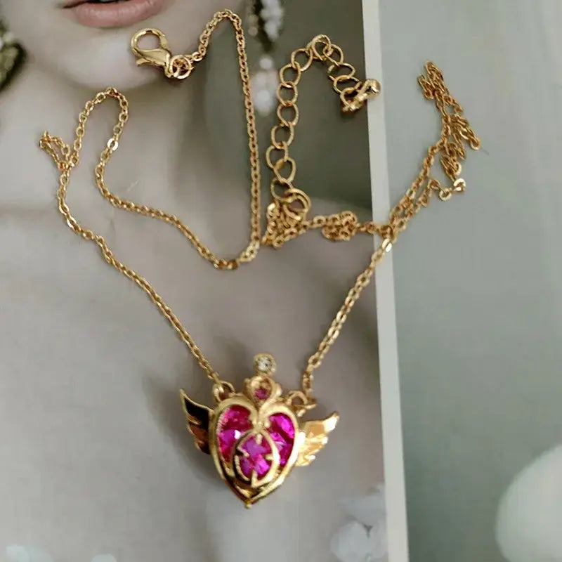 Gold-toned sailor moon tsukino necklace set with heart-shaped pink gemstone pendant and angel wing details