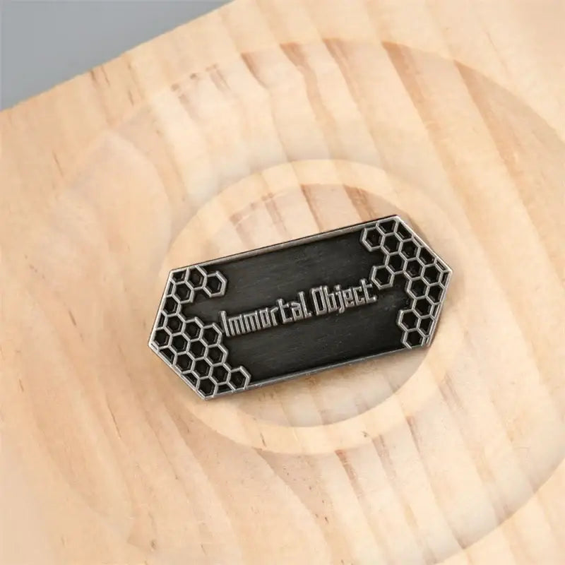 A sleek black and silver hexagonal sword art online emaille pin with honeycomb edges and immortal object engraving