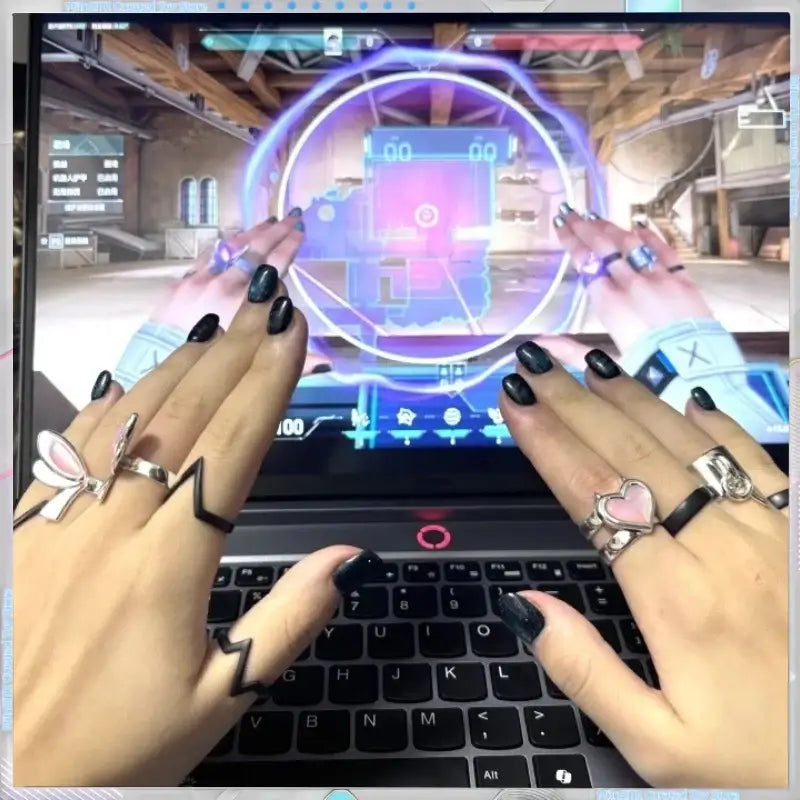 Hands with black nail polish wearing valorant clove adjustable ring set on a black laptop keyboard close-up