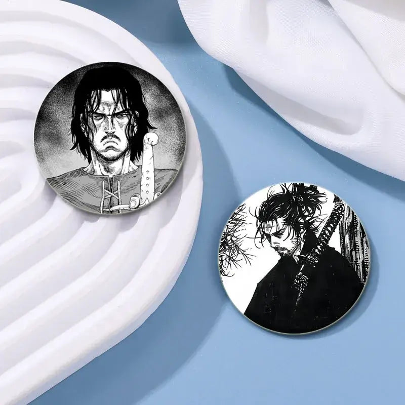 Two black-and-white tinplate anime badge pins featuring a warrior and samurai from vinland saga in 32 44 58mm sizes