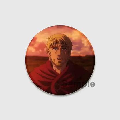 Circular vinland saga badge pin featuring a blonde anime character in a red cloak against an orange sunset background