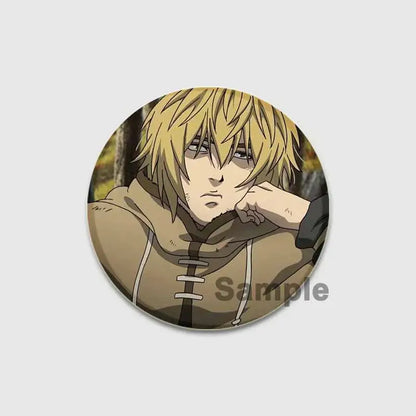 Circular vinland saga badge pin featuring an anime character with blonde hair in a tan hooded garment on tinplate