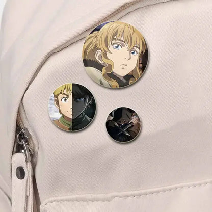 Three circular vinland saga thorfinn button brooch pins with detailed tinplate illustrations on light fabric surface