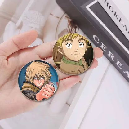 Two handmade circular vinland saga thorfinn enamel pins featuring a blonde boy and a spiky-haired figure on enamel