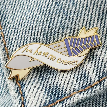 Gold-toned vinland saga thorfinn enamel pin shaped like a ribbon with purple white stripes and cursive phrase you have no enemies