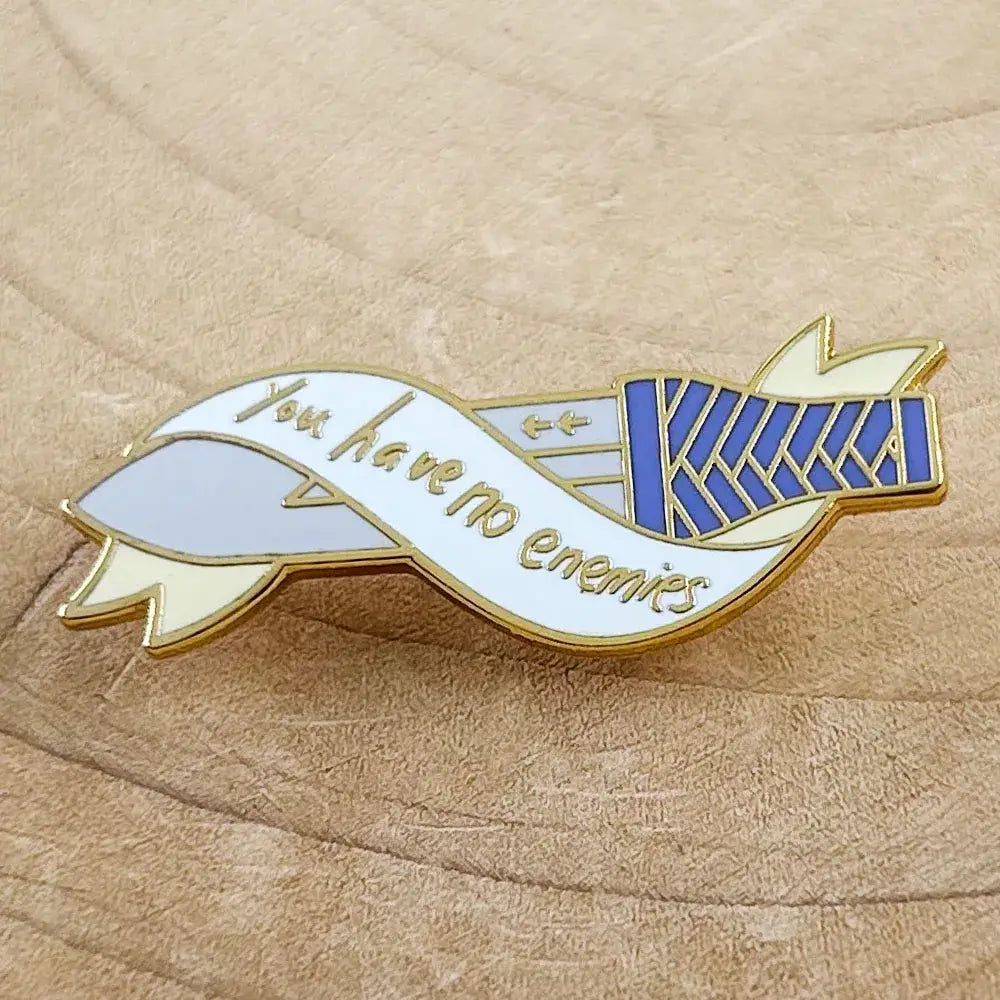 Vinland saga thorfinn enamel pin featuring a gold-trimmed white ribbon with you have no enemies and blue silver banner