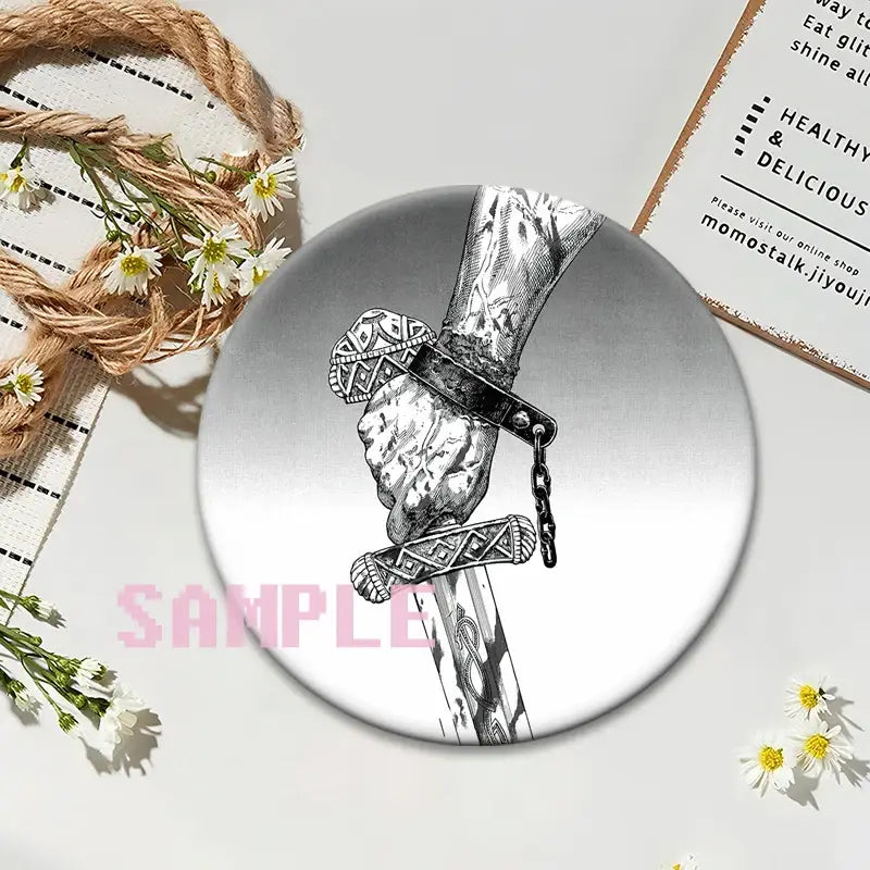 Circular silver vinland saga thorfinn lapel pin featuring a black and white tattooed hand gripping a sword with ornate hilt
