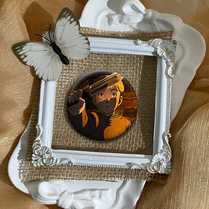 White ornate frame holding a circular vinland saga thorfinn lapel pin with gold and orange details on burlap backing