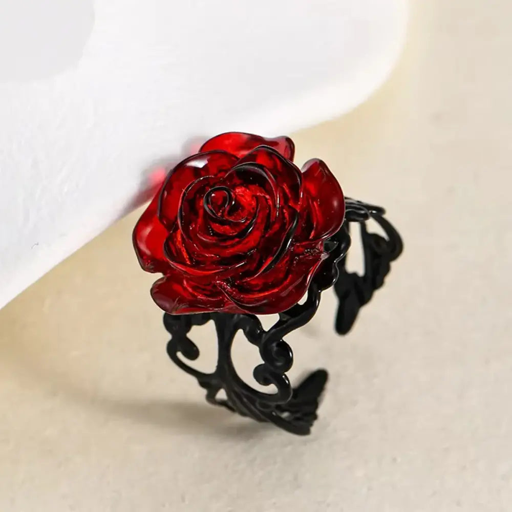 A gothic vintage vine ring with a striking red rose made of glass on a black ornate metal band