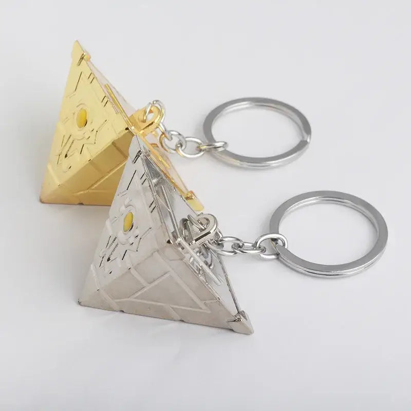 Two pyramid-shaped alloy keychains in gold and silver with detailed engravings and yellow gemstones for pendant necklace use
